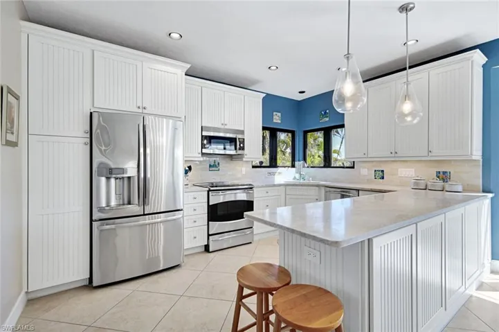 Kitchen with stainless steel appliances, a peninsula, white cabinetry, and light tile patterned floors