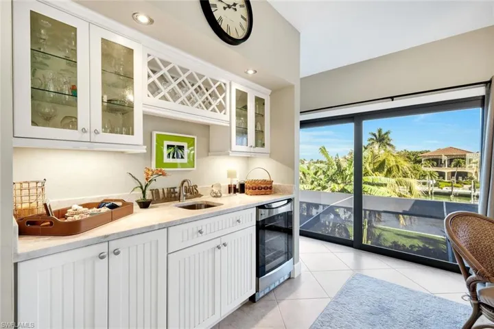 Indoor wet bar featuring white cabinets, light stone counters, light tile patterned flooring, glass fronted cabinets, and recessed lighting
