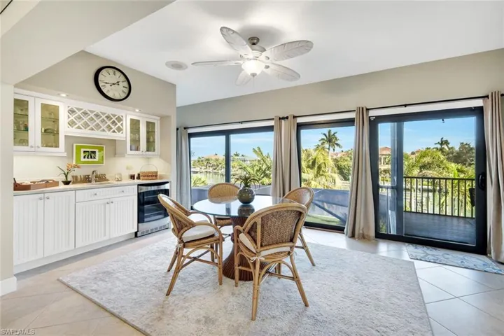 Dining space with light tile patterned floors, a ceiling fan, wine cooler, vaulted ceiling, and bar area