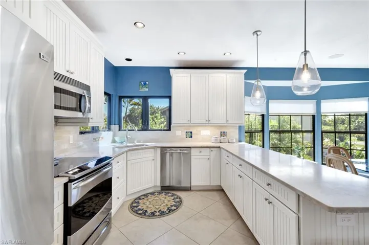 Kitchen featuring stainless steel appliances, white cabinets, a peninsula, light tile patterned floors, and decorative light fixtures