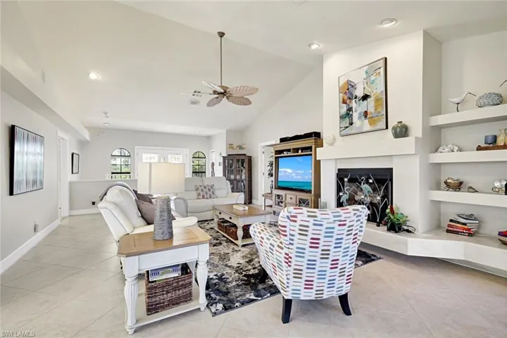 Living room featuring a ceiling fan, a fireplace with raised hearth, light tile patterned flooring, lofted ceiling, and recessed lighting