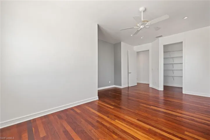 Unfurnished room featuring visible vents, built in shelves, baseboards, a ceiling fan, and wood-type flooring