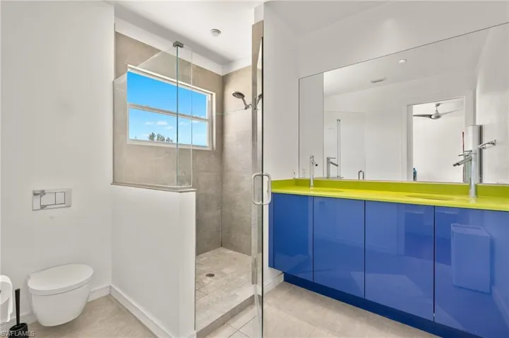 Bathroom with tile patterned floors, toilet, a shower stall, double vanity, and baseboards