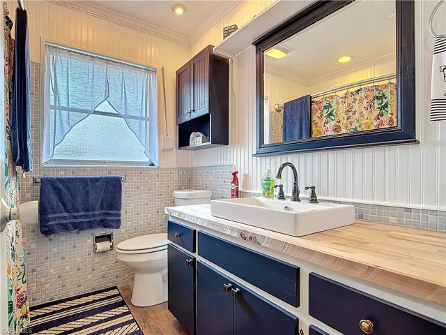 Bathroom with toilet, ornamental molding, tile walls, and vanity