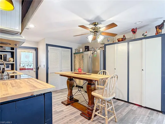 Kitchen with black electric cooktop, blue cabinets, wood counters, freestanding refrigerator, and light wood finished floors