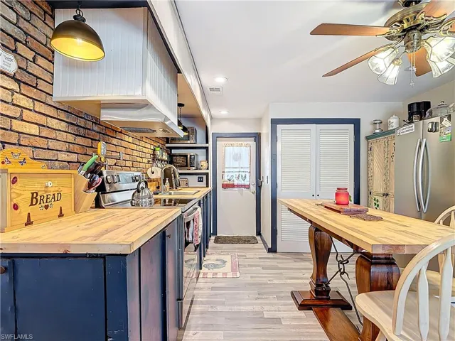 Kitchen featuring stainless steel appliances, butcher block counters, light wood-style floors, and brick wall