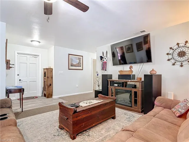 Carpeted living room with baseboards, visible vents, and a ceiling fan