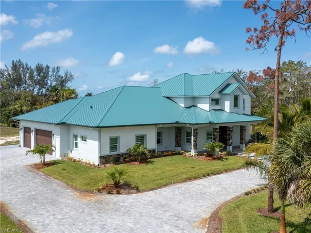 View of front of home featuring a garage, a front lawn, stone siding, metal roof, and decorative driveway