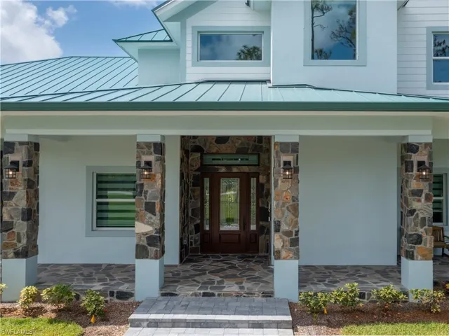 Doorway to property with a standing seam roof, stone siding, metal roof, and covered porch