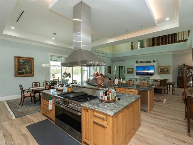 Kitchen with double oven range, a raised ceiling, island exhaust hood, a center island, and crown molding