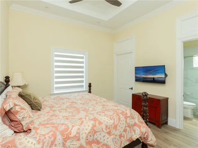 Bedroom featuring crown molding, wood finished floors, ensuite bath, a raised ceiling, and baseboards