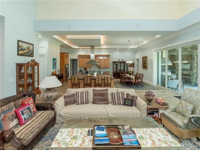 Living room with a raised ceiling, ornamental molding, light wood-style floors, recessed lighting, and baseboards