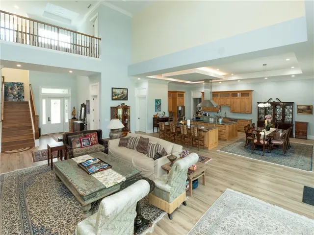 Living room with light wood-type flooring, stairway, a raised ceiling, crown molding, and recessed lighting