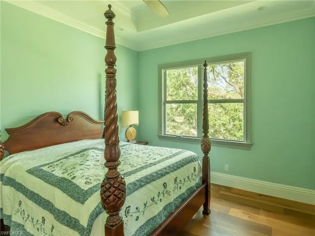 Bedroom featuring baseboards, wood finished floors, a tray ceiling, and ornamental molding