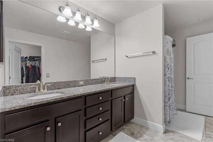 Full bathroom featuring marble look tile flooring, double vanity, a walk in closet, and baseboards