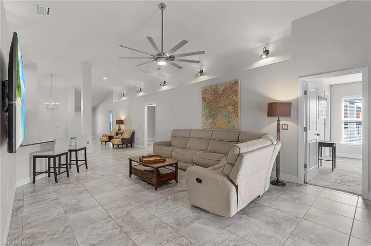 Living area featuring vaulted ceiling, ceiling fan, baseboards, and light marble finish flooring