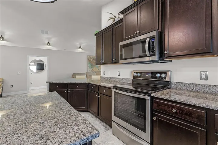 Kitchen with appliances with stainless steel finishes, dark brown cabinets, light stone counters, a peninsula, and baseboards