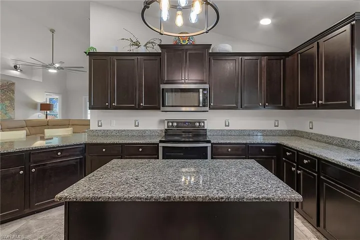 Kitchen featuring appliances with stainless steel finishes, lofted ceiling, ceiling fan, a kitchen island, and light stone counters