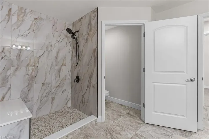 Full bathroom featuring a marble finish shower, marble look tile flooring, toilet, and baseboards