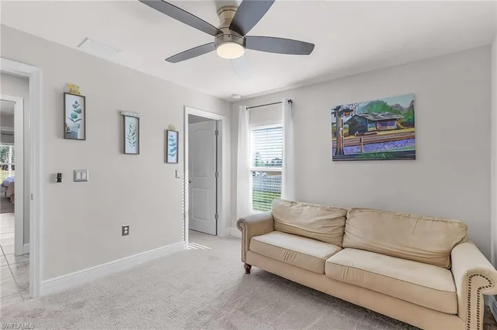 Living area with a ceiling fan, plenty of natural light, baseboards, and light carpet