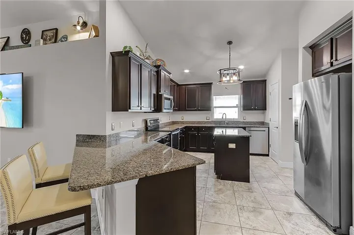 Kitchen with stainless steel appliances, a peninsula, a sink, dark brown cabinetry, and stone counters