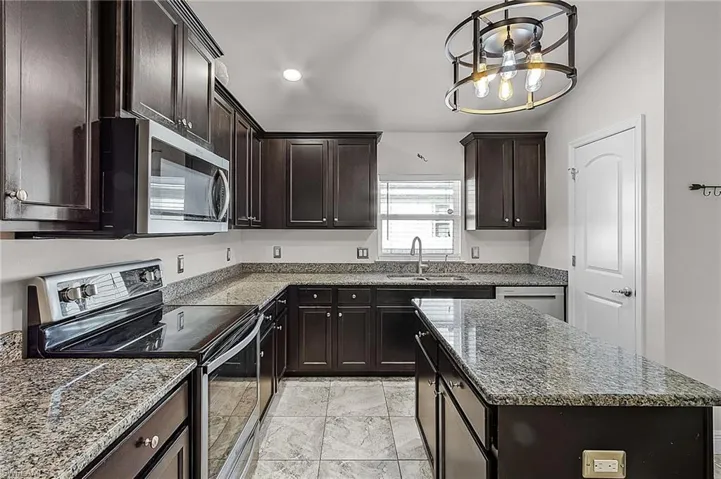 Kitchen featuring stainless steel appliances, a sink, stone counters, a kitchen island, and recessed lighting