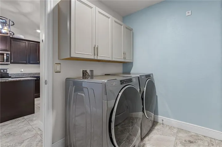 Laundry room with light marble finish floors, independent washer and dryer, cabinet space, and baseboards