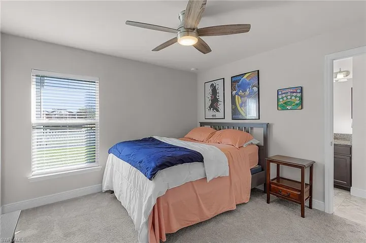 Bedroom with baseboards, light colored carpet, ensuite bath, and a ceiling fan