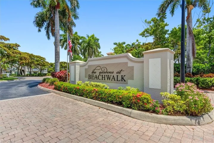 Entry monument featuring "The Gardens at Beachwalk" inscription, flanked by lush landscaping and mature palm trees