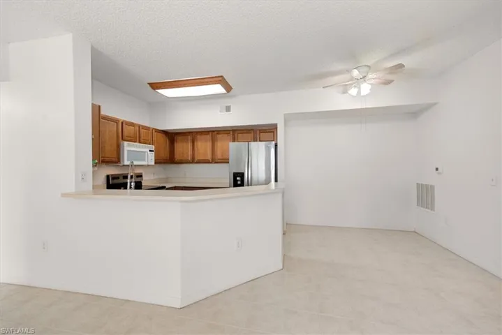 Open-concept kitchen and dining area featuring warm wood cabinetry, stainless steel appliances, a breakfast bar, and tile flooring