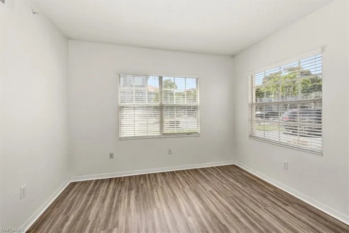 Bright interior space featuring wood-finish flooring, two windows with blinds, white walls, and white trim