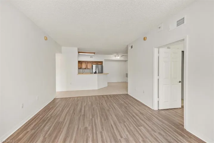 Spacious room with wood-finish flooring, white painted walls, and a textured ceiling