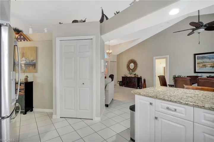 Kitchen featuring stainless steel fridge, white cabinets, light tile patterned floors, ceiling fan, and light stone counters