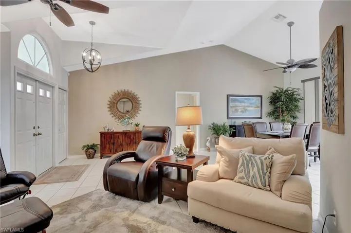 Tiled living room featuring ceiling fan with notable chandelier and high vaulted ceiling