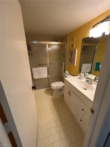 Bathroom featuring toilet, a textured ceiling, vanity, a shower with door, and tile patterned flooring