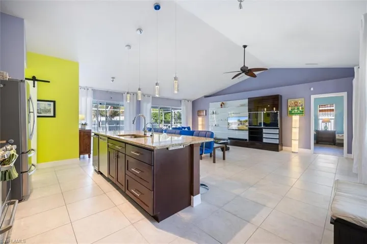 Kitchen featuring lofted ceiling, pendant lighting, dark brown cabinets, a center island with sink, and open floor plan