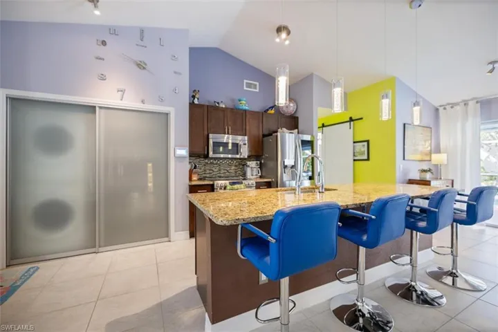Kitchen with dark brown cabinets, a kitchen bar, tasteful backsplash, appliances with stainless steel finishes, and light stone countertops