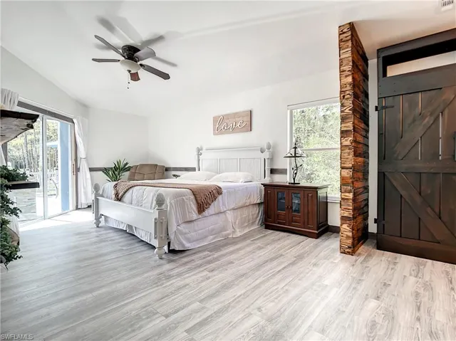 Bedroom with light wood-style flooring, access to outside, ceiling fan, multiple windows, and lofted ceiling