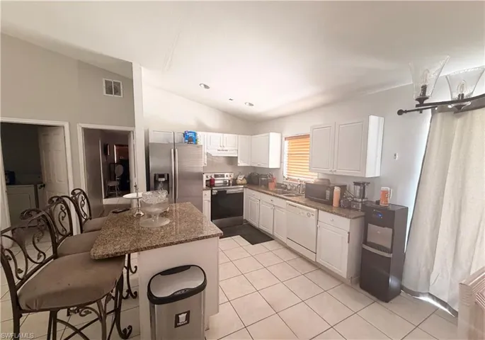 Kitchen featuring white cabinetry, light-toned countertop, stainless steel appliances, and tile flooring