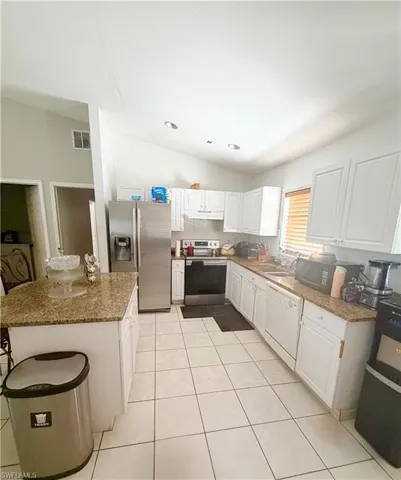 Modern kitchen featuring white cabinetry, granite-finish countertops, stainless steel appliances, and tile flooring