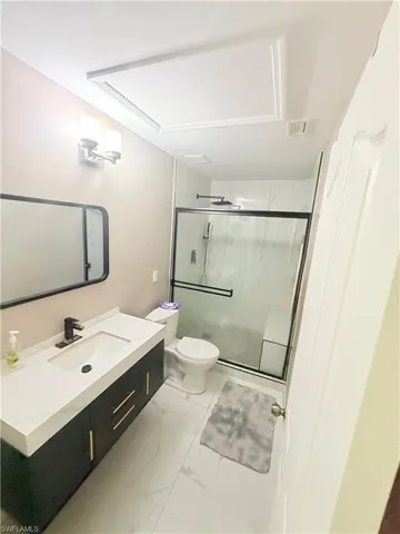 Floating vanity with integrated sink and matte black faucet, glass-enclosed shower with contrasting frame, wall-mounted light fixture, and white tile flooring