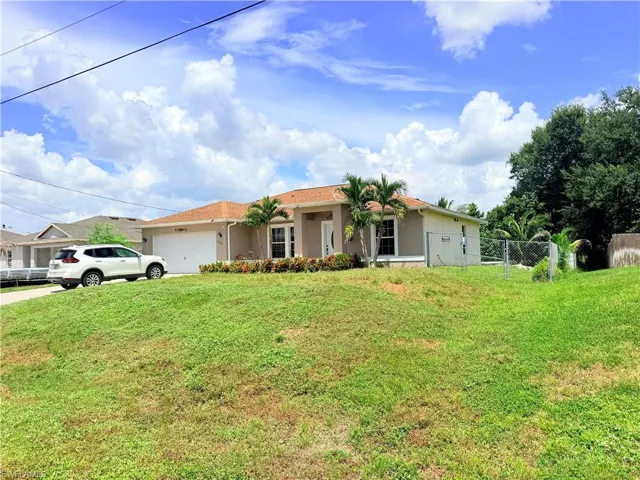 Stucco exterior residence with an attached garage, paved driveway, and mature landscaping