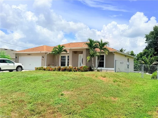 Single-story residence featuring a two-car garage, established palm trees, and a chain-link fence