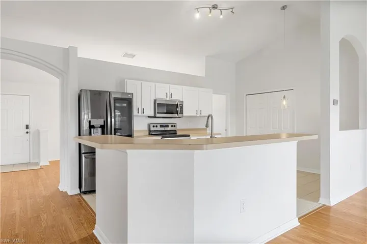 Kitchen with light hardwood / wood-style flooring, stainless steel appliances, a center island with sink, rail lighting, and white cabinets