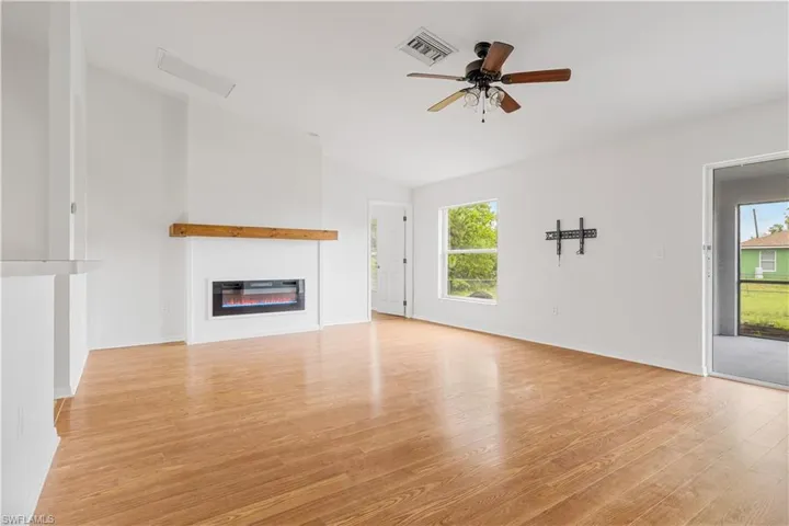 Living room featuring electric fireplace, vaulted ceiling, ceiling fan, and light hardwood / wood-style flooring