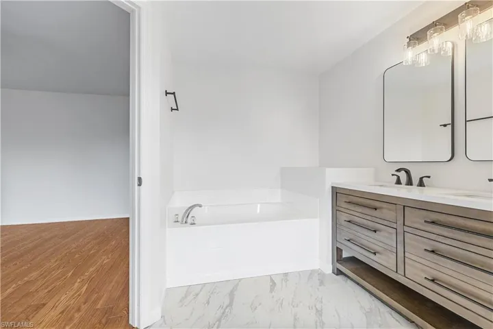 Bathroom featuring a large soaking tub, wood-type flooring, and vanity with extensive cabinet space
