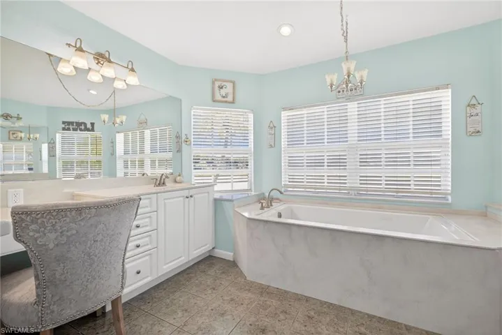 Built-in vanity with white cabinetry, integrated soaking tub, tiled flooring, and multiple windows with blinds
