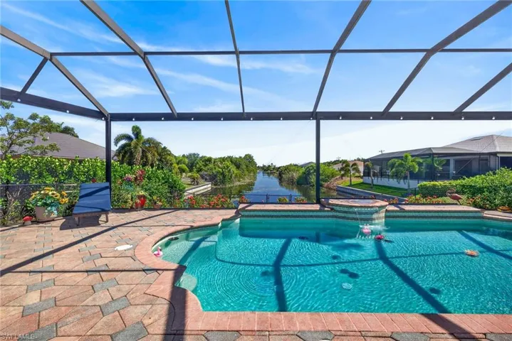 Screened-in outdoor living space featuring a freeform pool with integrated spa, paver patio, and canal access