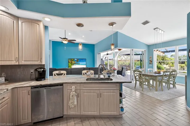 Kitchen island with integrated sink, stainless steel dishwasher, wood-finish cabinetry, and light-toned countertop