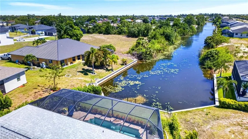 Waterfront property featuring a sparkling saltwater pool with retractable enclosure, expansive lanai with composite decking, manicured lawn, and direct waterfront access with dock